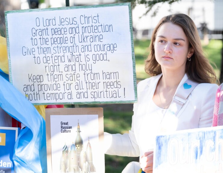 Kvinde med skilt hvor der står "O Lord Jesus Christ Grant peace and protection to the people of Ukraine. Give them strength and courage to defend what is good, right, and holy. Keep them safe from harm and provide for all their needs both temporal and spiritual!"